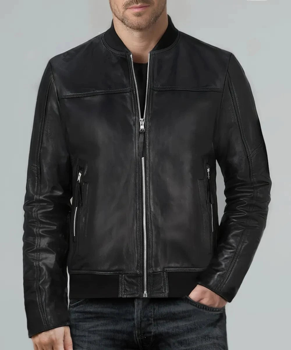 Male model wearing a black leather Legacy bomber jacket with slim fit styling, ribbed band collar, silver zip front closure, zip side pockets, and minimalist leather panel detailing paired with dark denim jeans